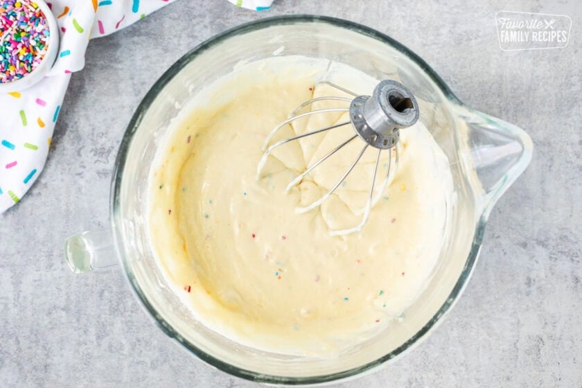 Glass mixing bowl with cake batter and a whisk attachment.