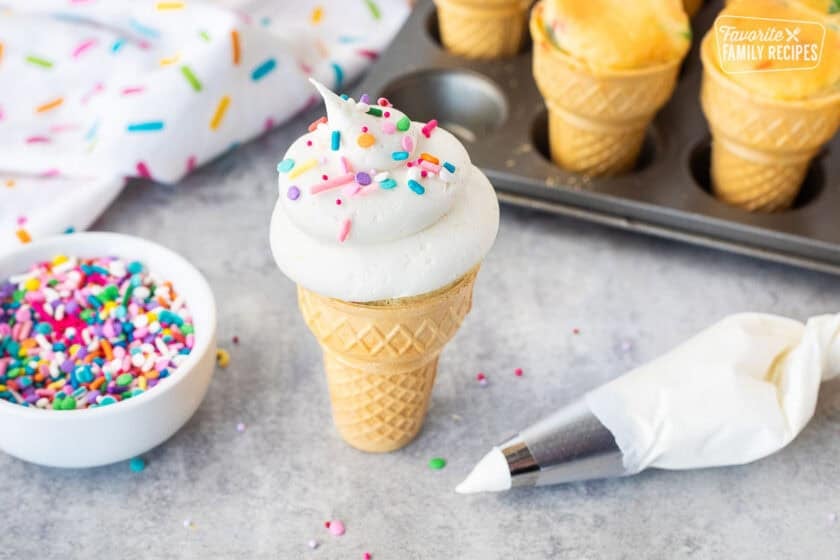 Frosted and decorated ice cream cone cupcakes. Piping bag and sprinkles on the side.