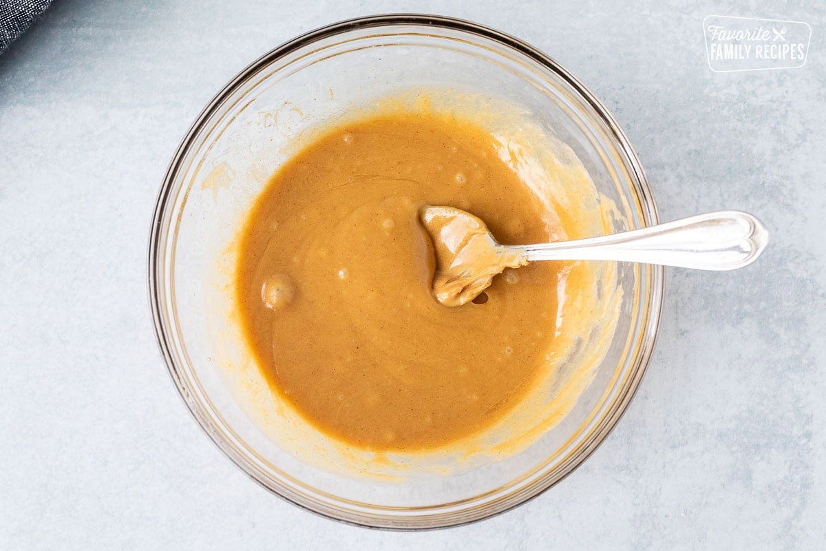 Glass bowl with creamy peanut butter and honey combined with a spoon.