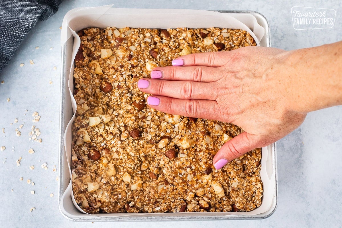 Pressing down Peanut Butter Granola Bars by hand into a baking pan lined with parchment paper.