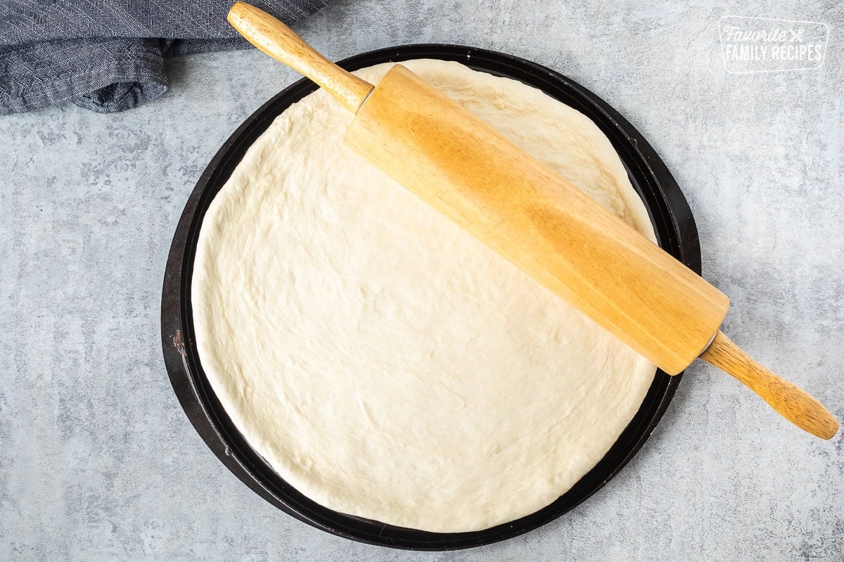 Pizza dough rolled out in a circle with a rolling pin.