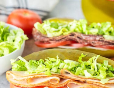 Two pickle sandwiches on a cutting board with turkey, lettuce, tomato, provolone cheese and cream cheese.
