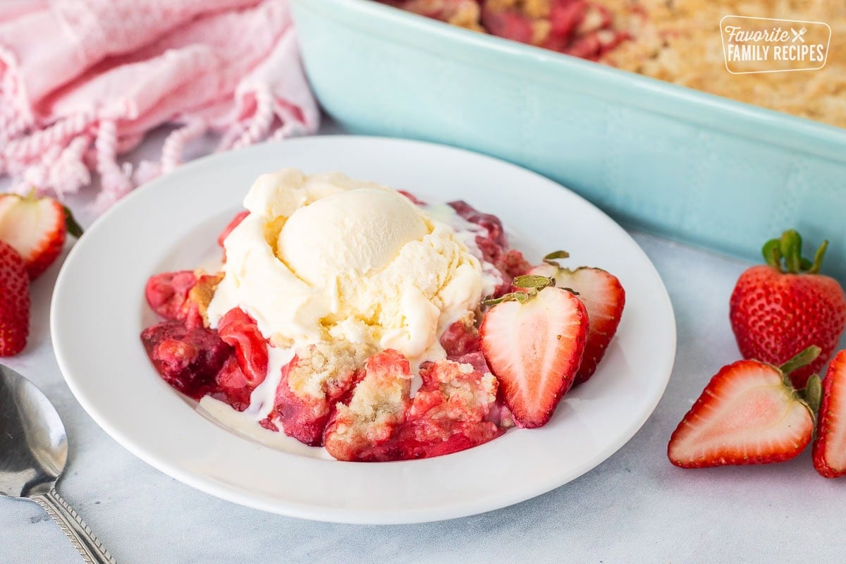 A serving dish of gooey Strawberry Cheesecake Dump Cake with a crumble cake topped with vanilla ice cream.