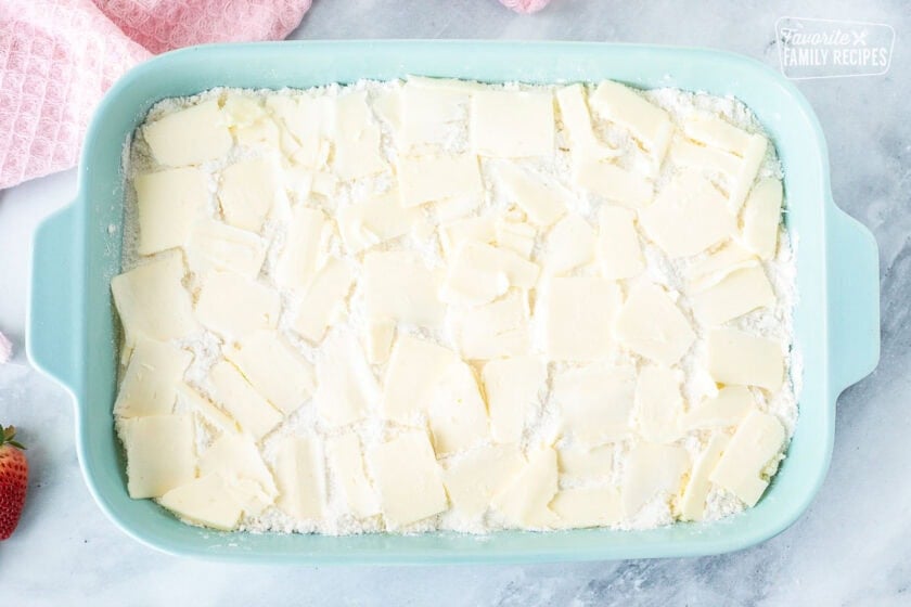 Thinly sliced butter on top of cake mix in a baking dish.