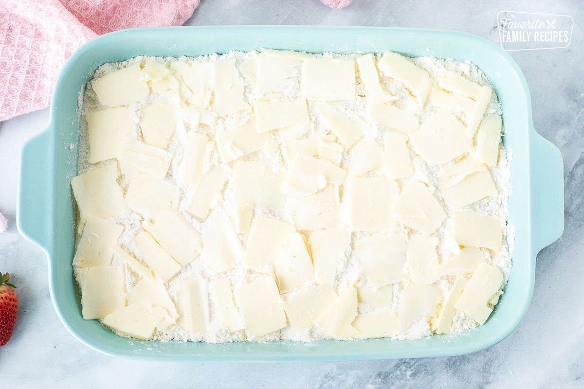 Thinly sliced butter on top of cake mix in a baking dish.
