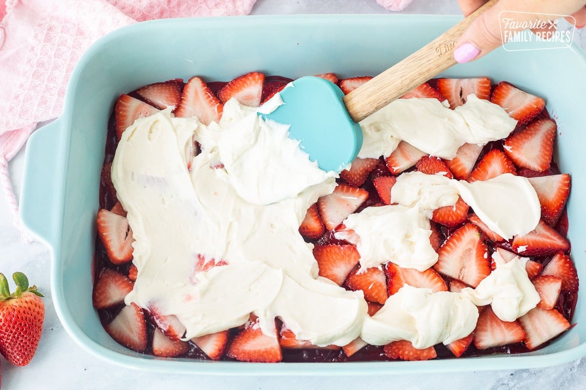 Spreading cream cheese layer on top of fresh strawberries in a baking dish.