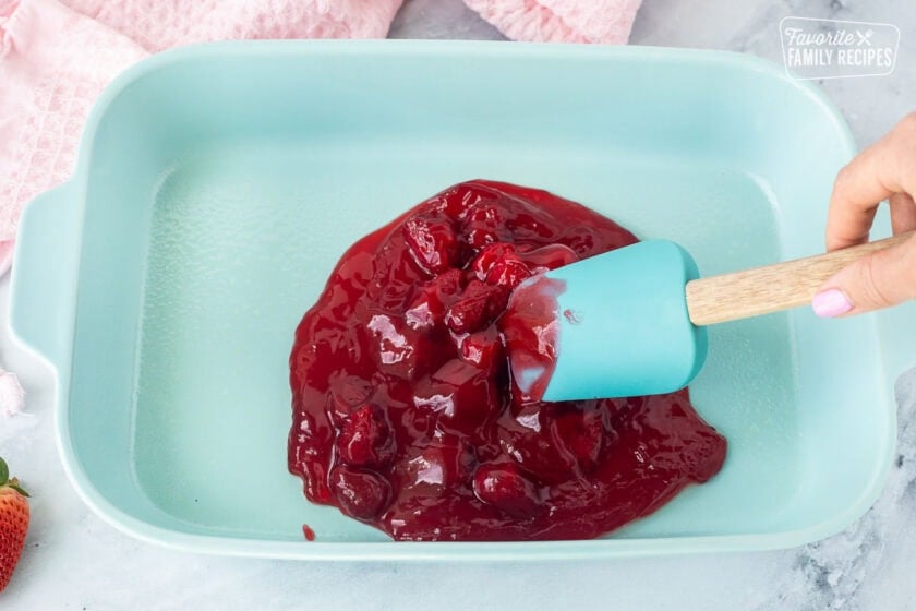 Spreading Strawberry pie filling in a baking dish.