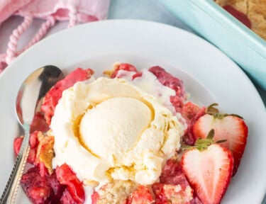 Strawberry Cheesecake Dump Cake on a plate topped with vanilla ice cream.