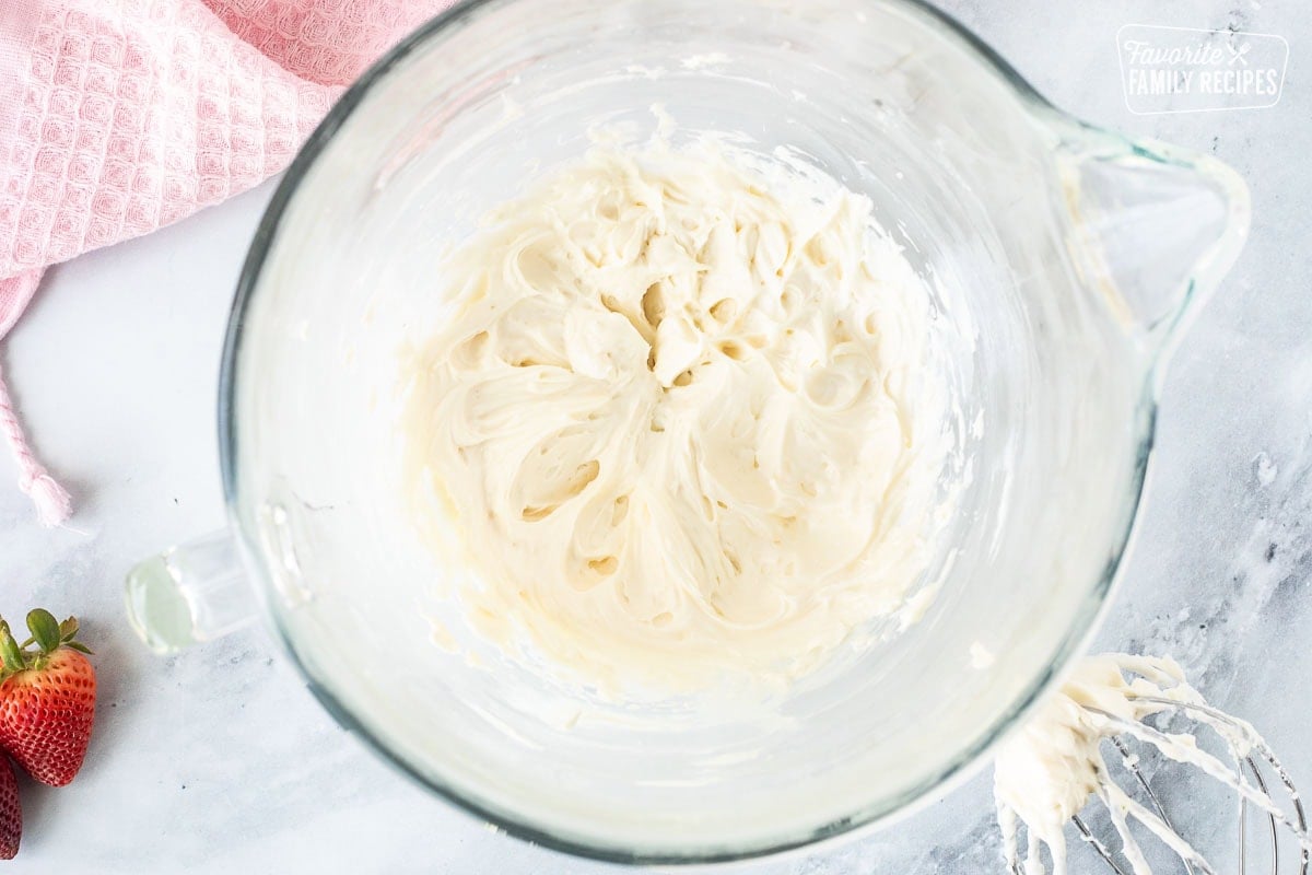 Glass mixing bowl with cream cheese mixture and whisk on the side.