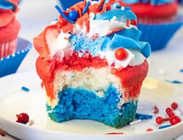 Bite out of a red, white and blue layered 4th of July Cupcakes with red, white and blue swirled frosting and sprinkles.
