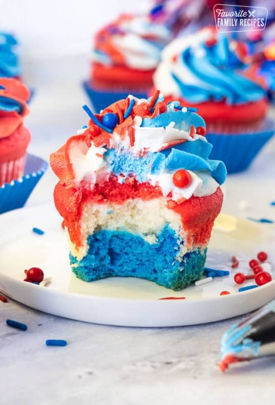 Bite out of a red, white and blue layered 4th of July Cupcakes with red, white and blue swirled frosting and sprinkles.