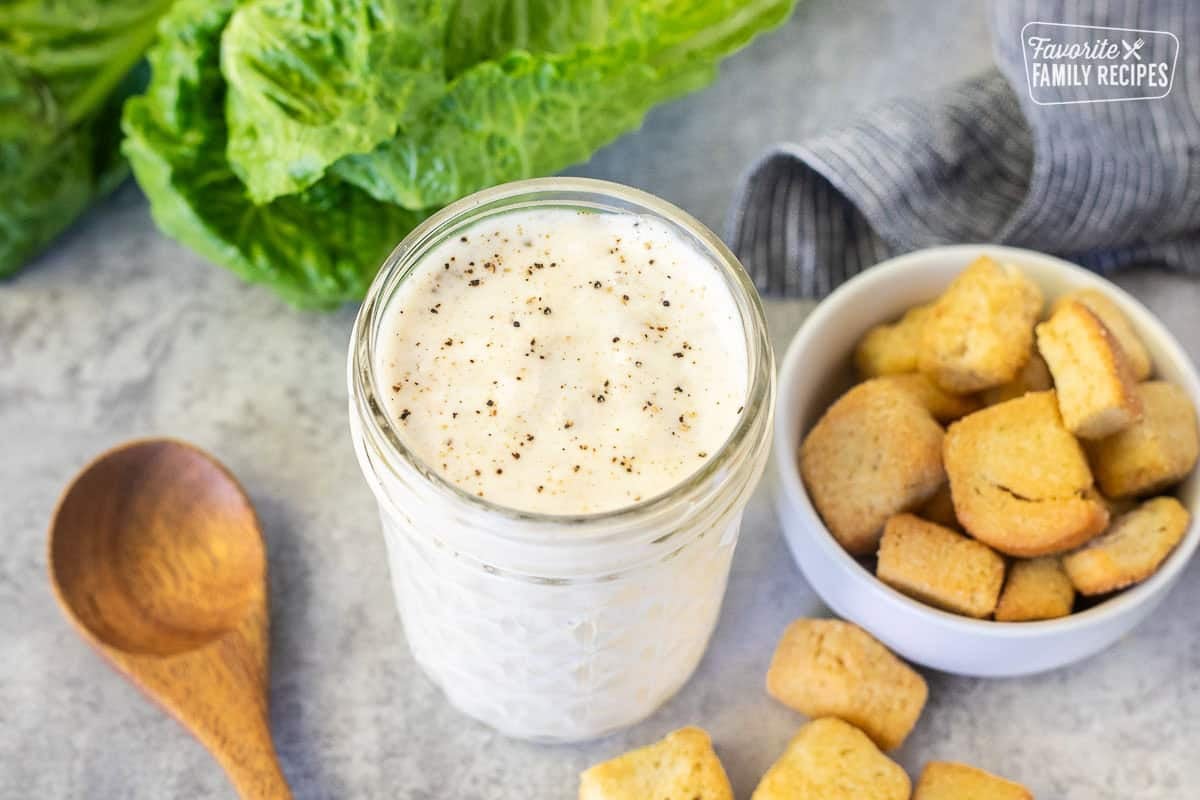 Jar of Caesar Salad dressing without anchovies. Romaine lettuce and croutons on the side.