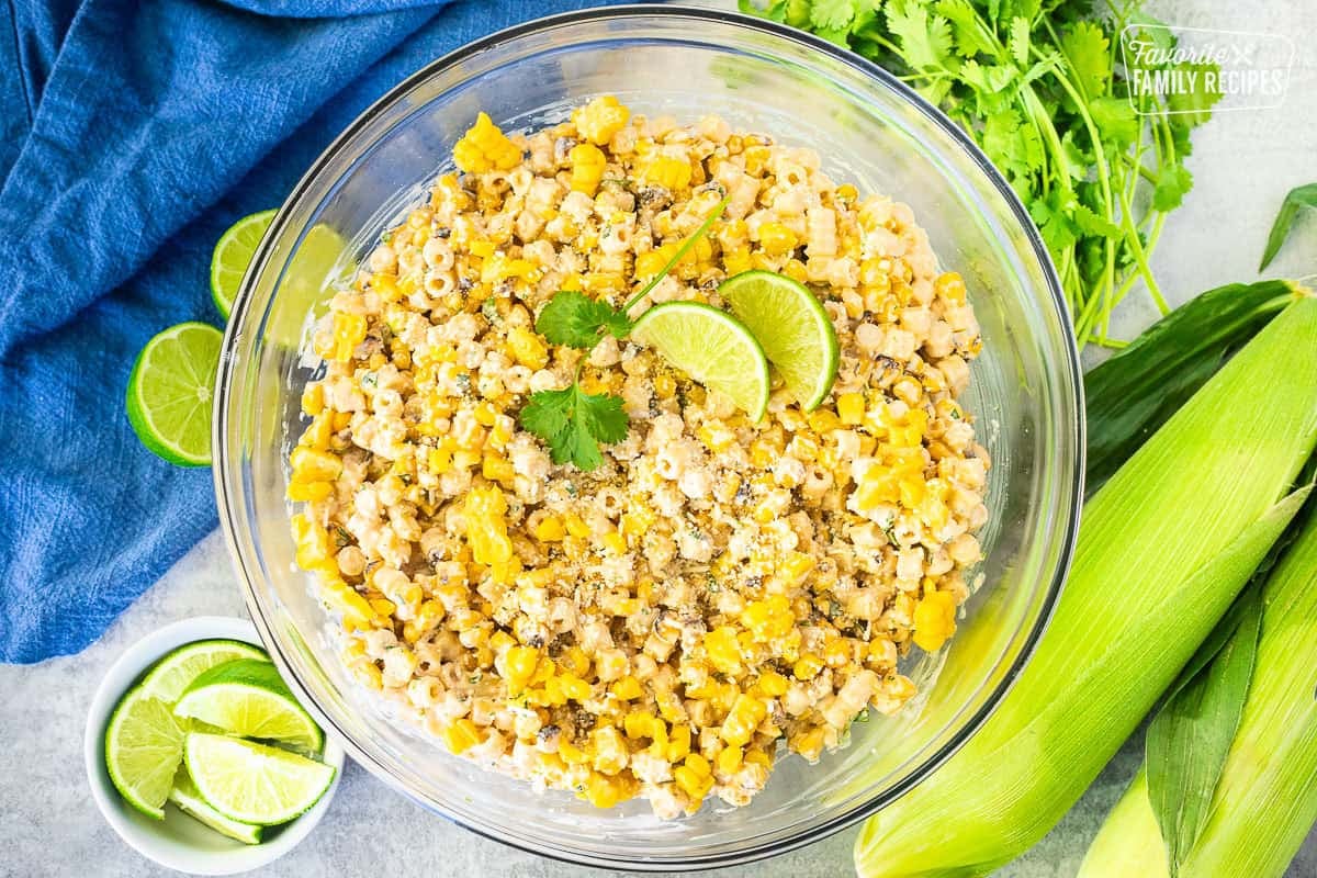 Glass mixing bowl with Elote Pasta Salad garnished with lime and cilantro.