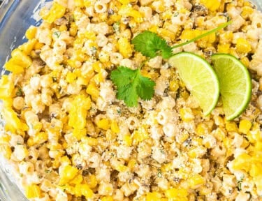 Glass mixing bowl with Elote Pasta Salad garnished with lime and cilantro.