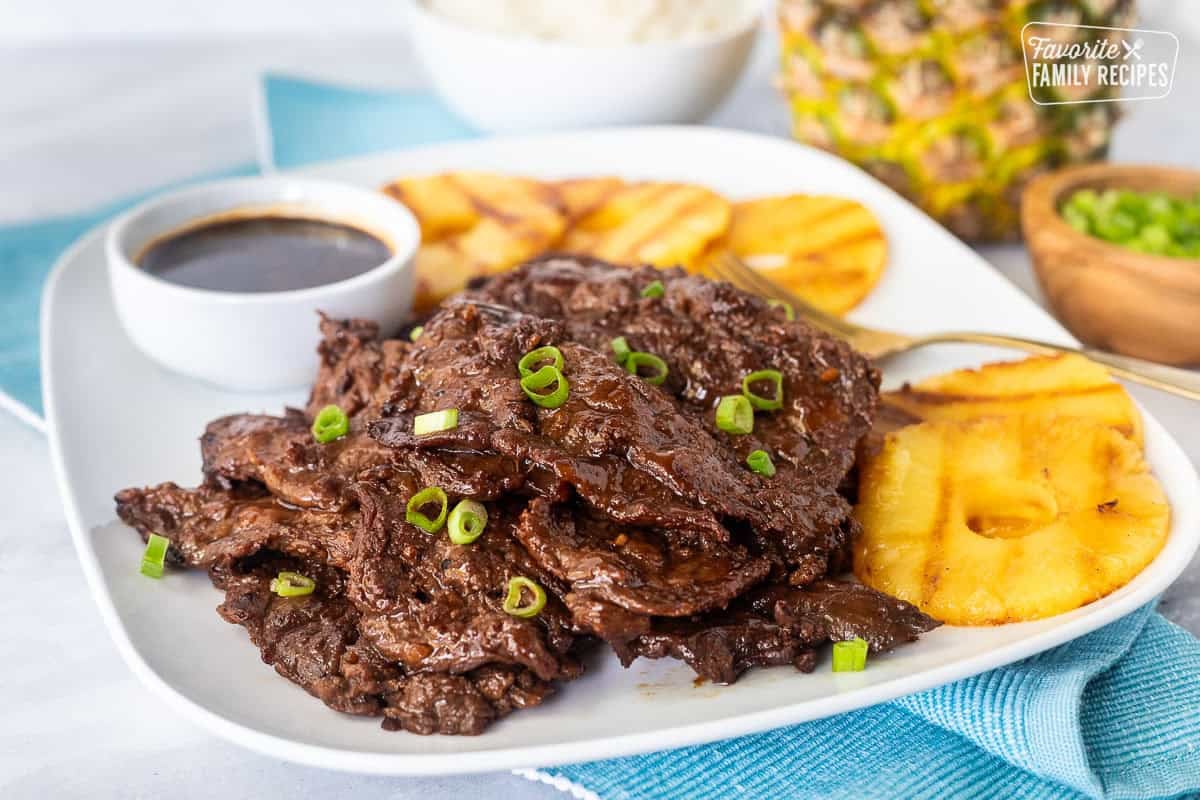 Hawaiian Beef Teriyaki on a plate garnished with green onion and grilled pineapple slices on the side.