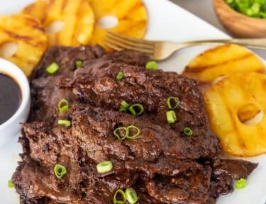 Hawaiian Beef Teriyaki on a plate garnished with green onion and grilled pineapple slices on the side.