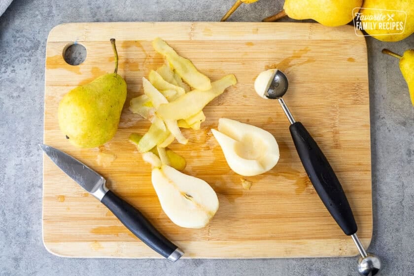 Cutting board with peeled fresh pear cut in half and melon baller used to remove the core.