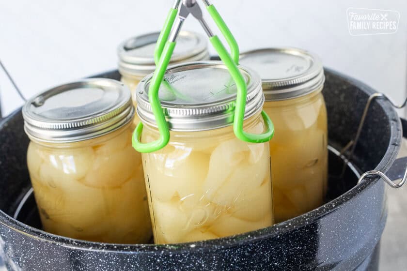Lifting processed canning jars with pears from large pot.