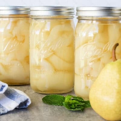 Four lined up canning jars of fresh pears.