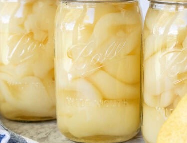 Canning jars lined up with fresh pears.