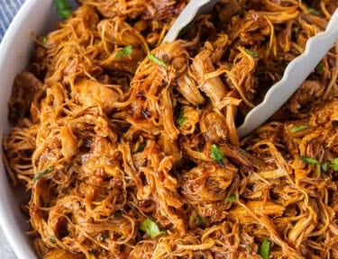 Instant Pot BBQ Chicken in a bowl with cilantro and tongs.