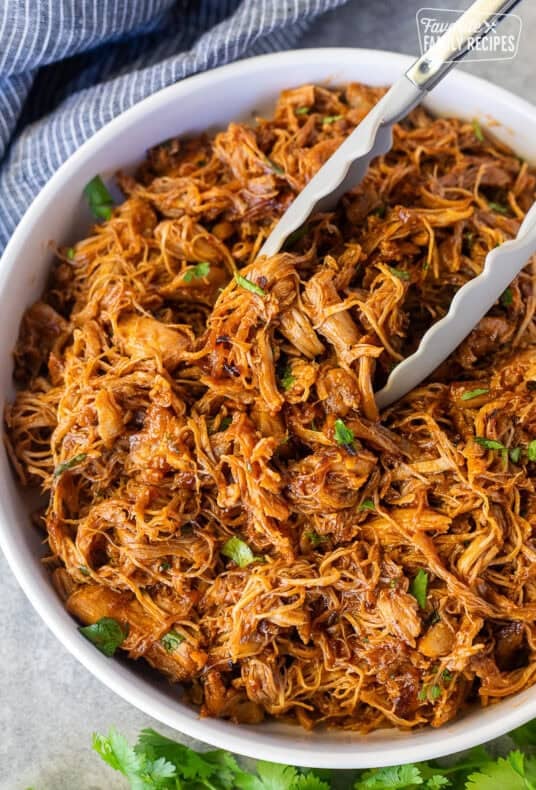 Instant Pot BBQ Chicken in a bowl with cilantro and tongs.