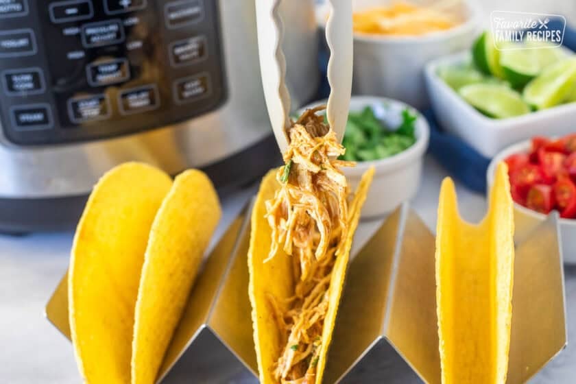 Placing Instant Pot chicken taco filling into a toco shell with tongs.