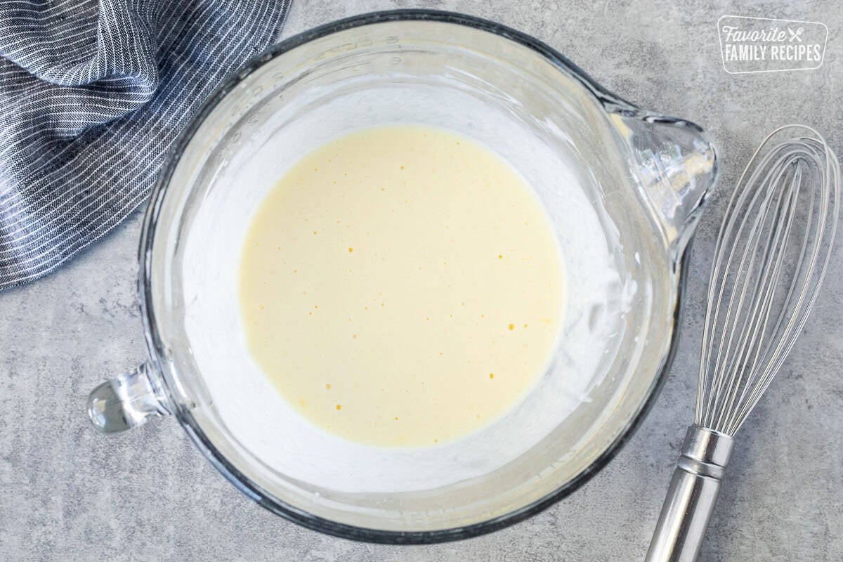 Glass mixing bowl with wet ingredients combined and whisk on the side.