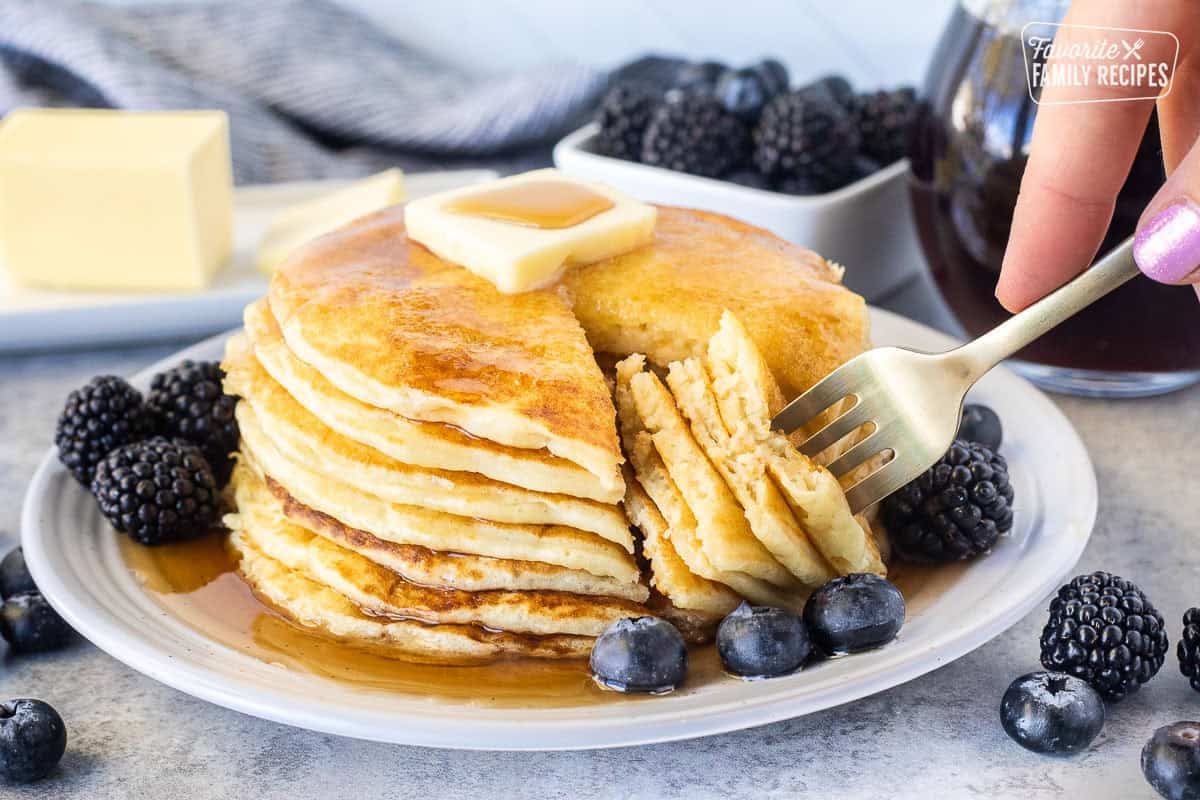 Fork with cut out pancakes from the stack of pancakes from scratch with maple syrup, blackberries and blueberries.