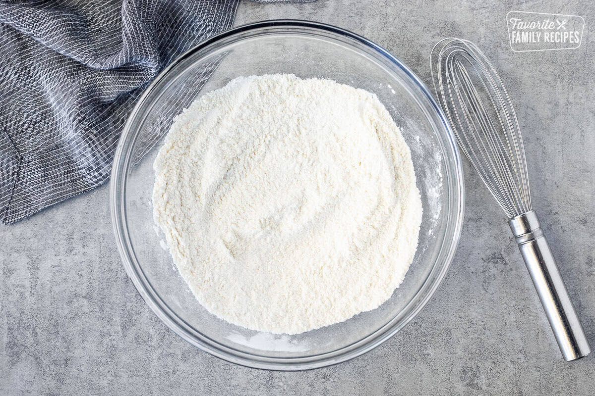 Glass mixing bowl with combined dry ingredients and whisk on the side.
