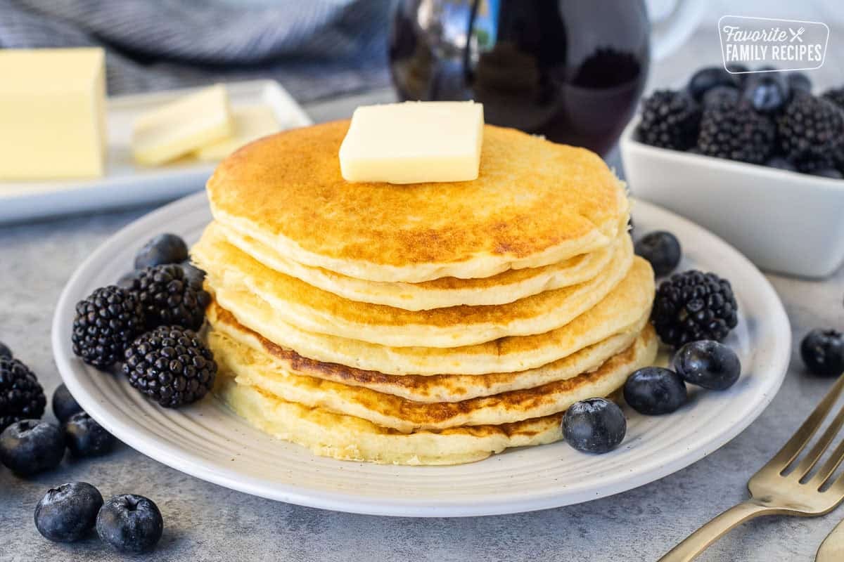 Stacked pancakes from scratch on a plate with a pad of butter. Syrup, blackberries and blueberries on the side.