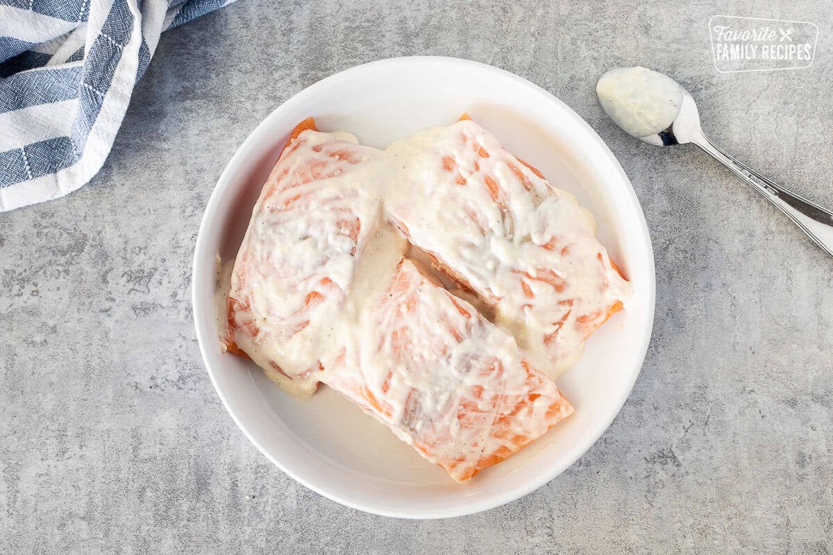 Salmon marinating with Caesar dressing in a shallow bowl. Spoon on the side.