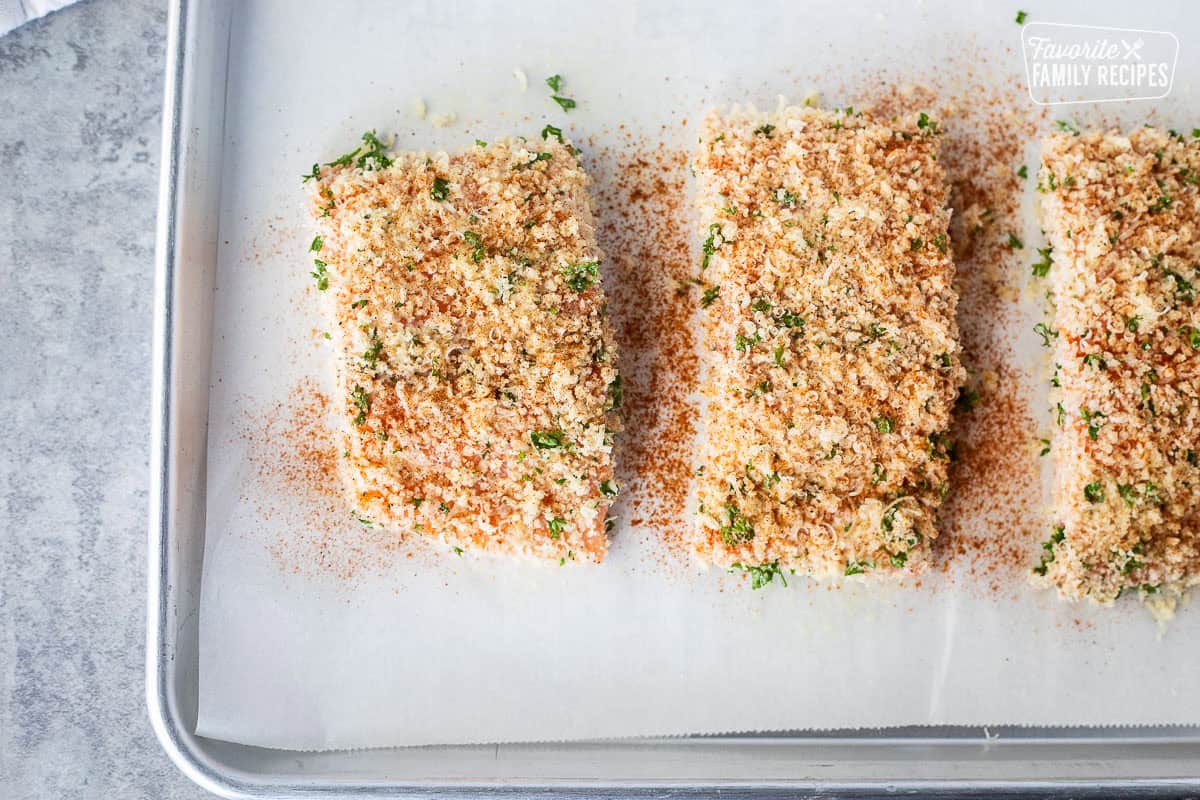 Uncooked salmon on parchment paper coated with panko mixture and seasoned with paprika.