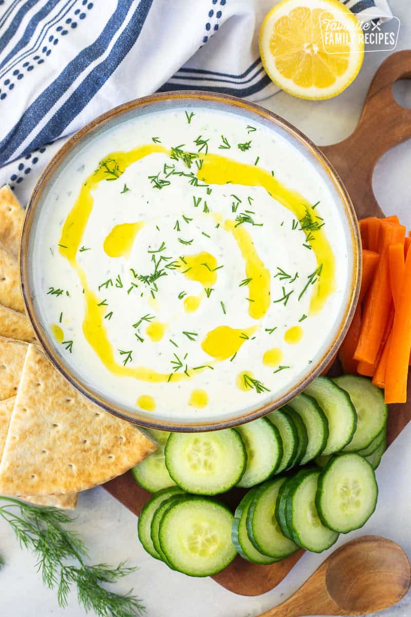 Tzatziki sauce in a bowl with olive oil and dill. Pita bread, cucumbers, carrot slices on the side.