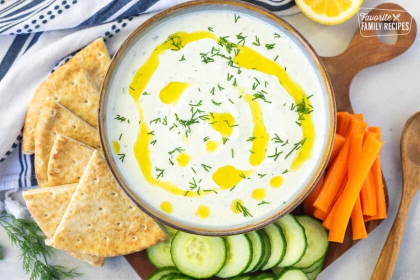 Tzatziki sauce in a bowl with olive oil and dill. Pita bread, cucumbers, carrot slices on the side.