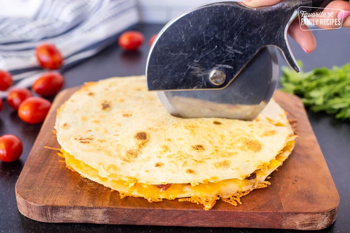 Cutting the Breakfast Quesadilla on a cutting board with a pizza cutter.