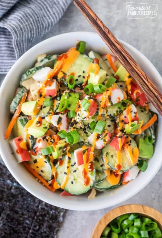 California roll cucumber salad with imitation crab, avocado, carrots, sesame seeds, green onions, and creamy sauce in a white bowl.