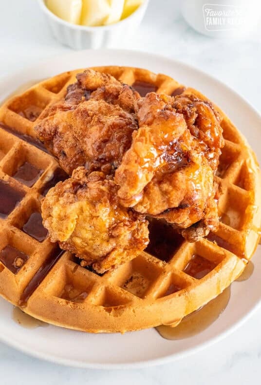 Round waffle with pieces of fried chicken on top with maple syrup. Butter and extra syrup on the side.