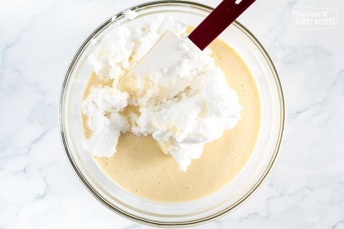 Glass mixing bowl with batter mix and spatula folding in the whipped egg whites.