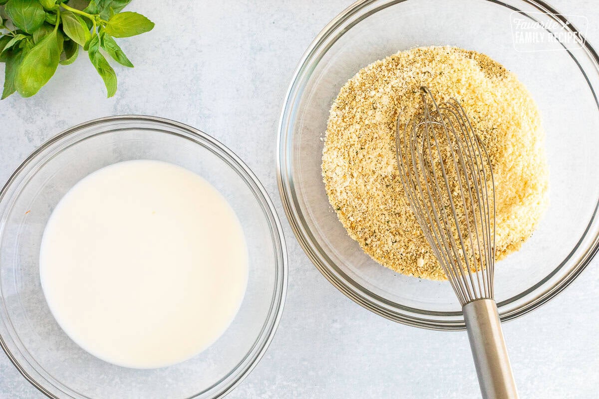 Bowl of breadcrumb mixture with a whisk next to a bowl of milk.