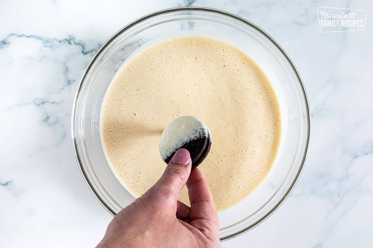 Dipping an Oreo cookie into a glass bowl of batter.