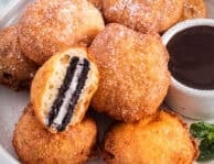 Deep fried Oreos next to a bowl of chocolate sauce. One Oreo cut in half.