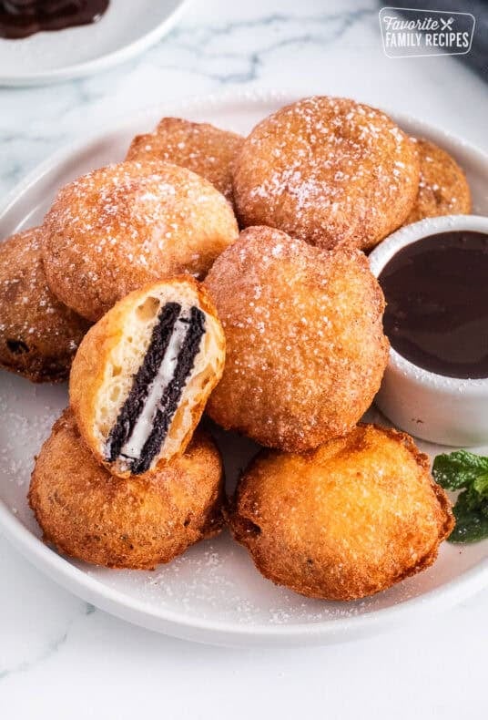 Deep fried Oreos next to a bowl of chocolate sauce. One Oreo cut in half.
