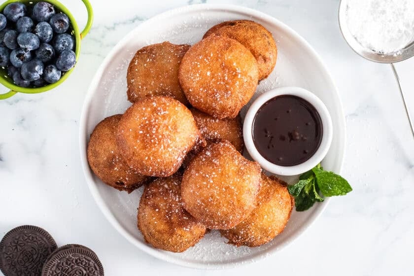 Deep fried Oreos next to a bowl of chocolate sauce.