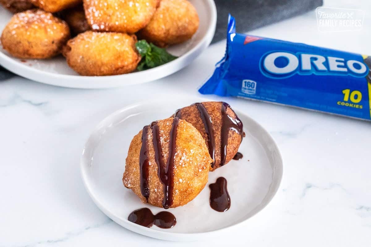 Deep fried Oreos drizzled with chocolate sauce on a plate.