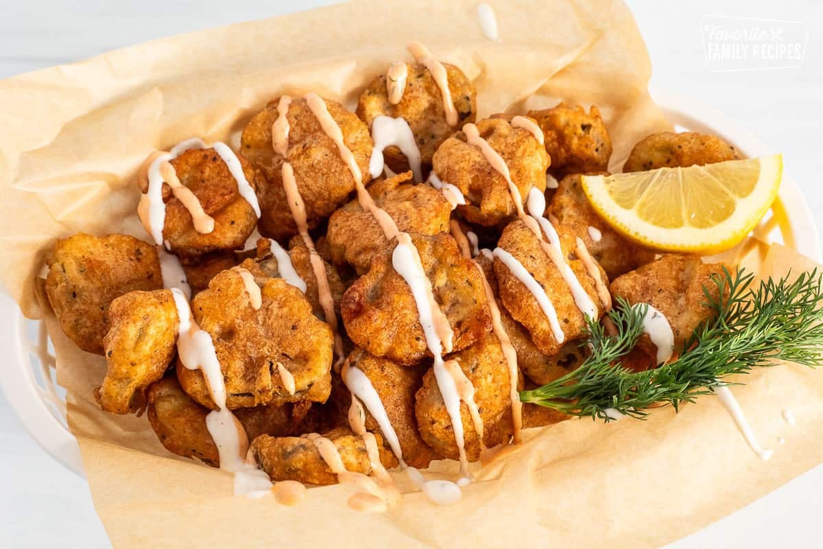 Fried pickles in a basket topped with Sriracha dill dipping sauce and ranch sauce.
