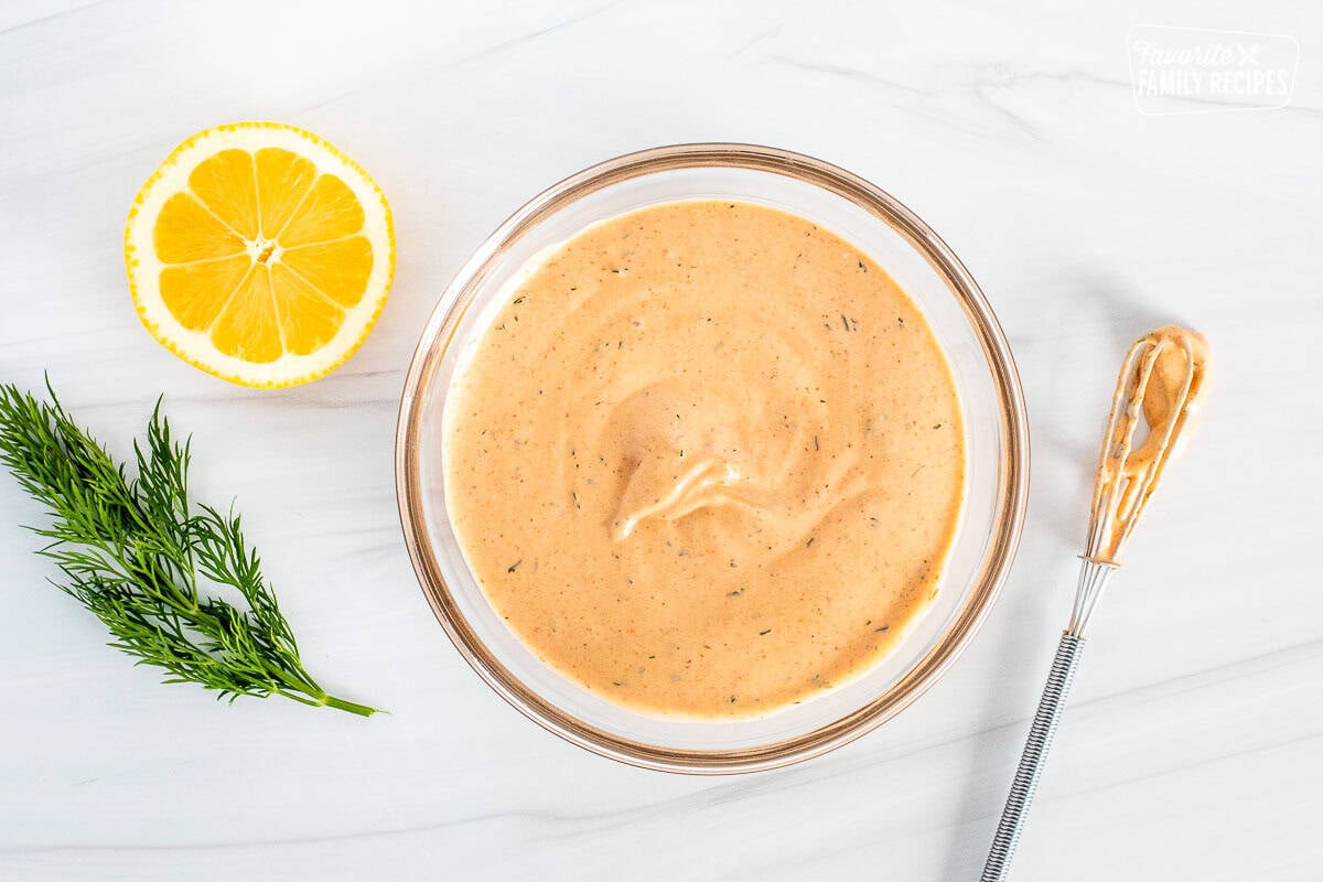 Glass mixing bowl with Sriracha Dill Dipping Sauce and whisk on the side.