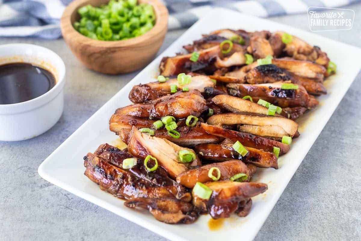 Hawaiian Grilled Teriyaki Chicken sliced on a dish and garnished with green onion. Extra onion and teriyaki sauce on the side.