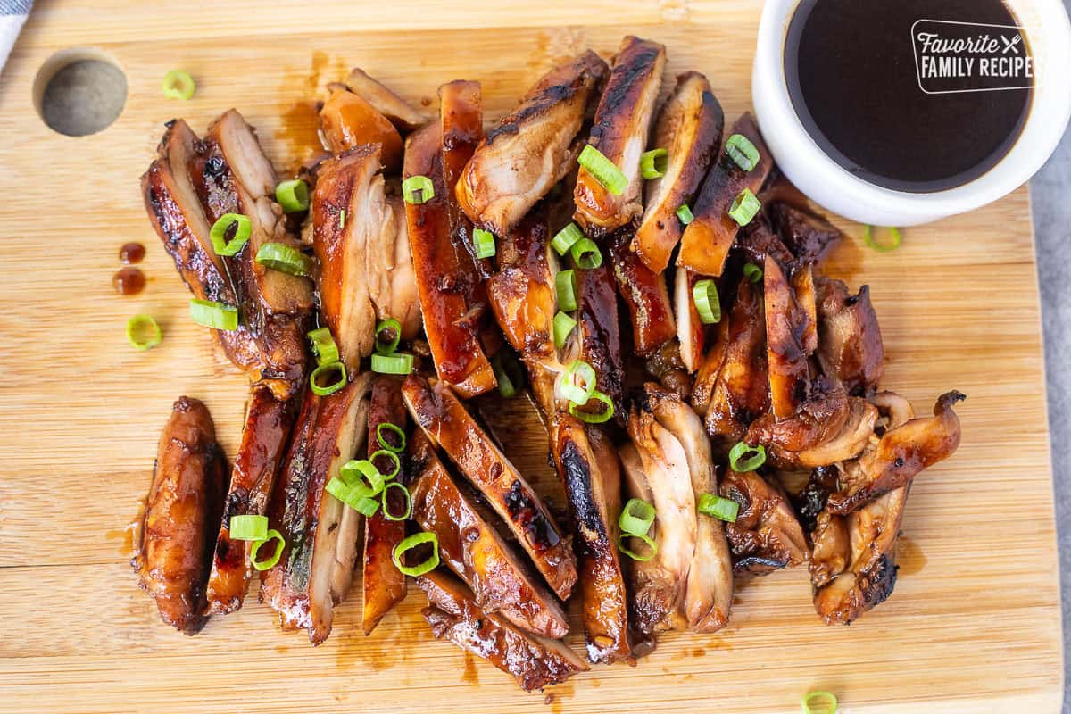 Hawaiian Grilled Teriyaki Chicken cut on a cutting board with a dish of teriyaki sauce and garnished with green onion.