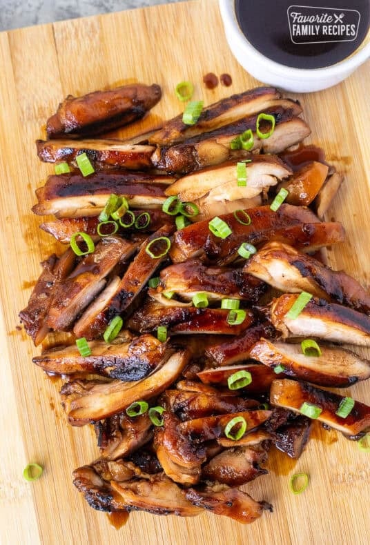 Hawaiian Grilled Teriyaki Chicken cut on a cutting board with a dish of teriyaki sauce and garnished with green onion.